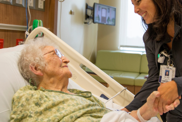 elderly patient in bed holding hands with nurse
