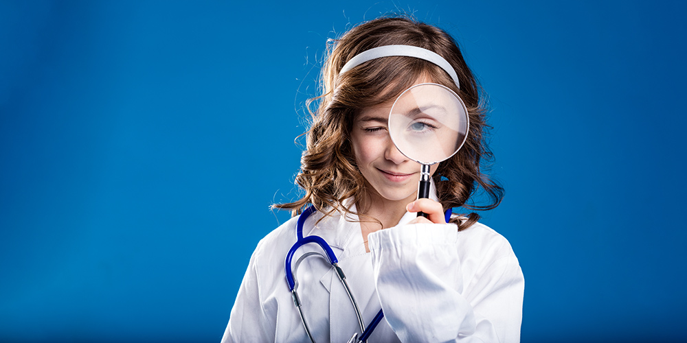 young girl dressed as a doctor looking through a magnifying glass